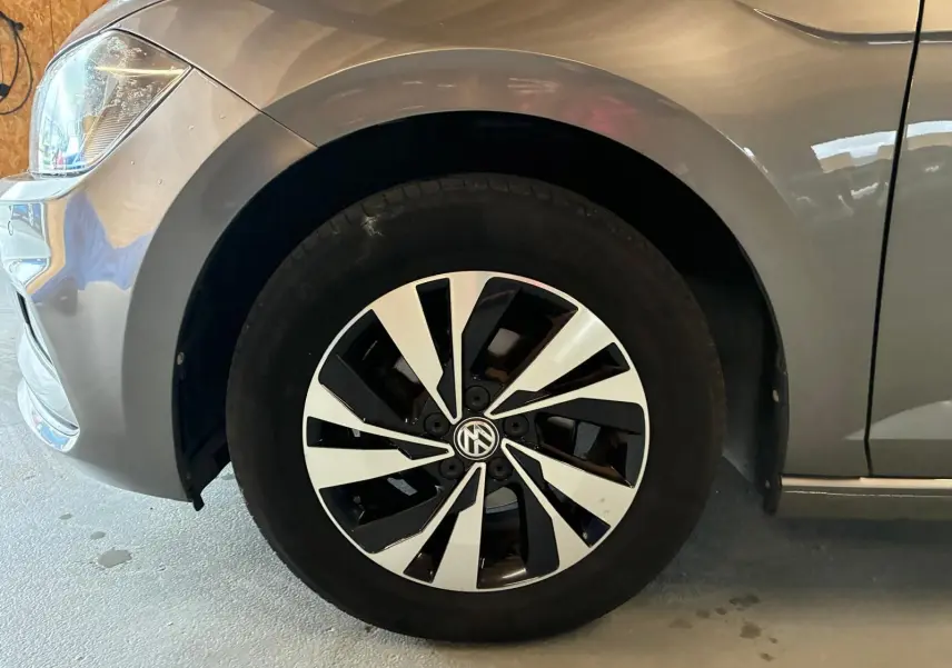 Gros plan sur la roue avant gauche d'une Volkswagen Polo gris métallisé avec jante noire et argentée au design moderne.