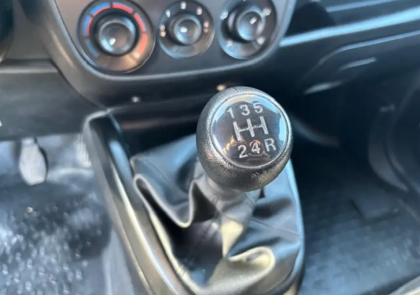 Gros plan sur le levier de vitesses manuel noir dans l’habitacle de l’Opel Combo blanc, avec commandes de climatisation en arrière-plan.