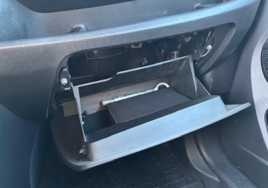 Gros plan sur la boîte à gants ouverte côté passager de l’Opel Combo blanc, montrant un outil et un carnet à l’intérieur.