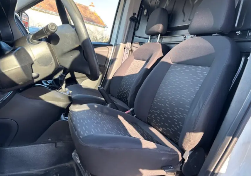 Vue intérieure côté conducteur de l’Opel Combo L1H1 2015, montrant les sièges avant en tissu gris et la cloison tôlée arrière.