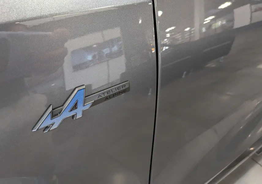 Gros plan sur l'emblème Atelier Alpine bleu sur la porte gris schiste du Renault Rafale hyper hybrid 2026.