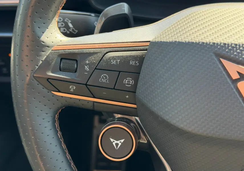 Gros plan sur le volant cuir perforé côté gauche du CUPRA Formentor gris métallisé avec commandes multifonctions et logo central cuivré.