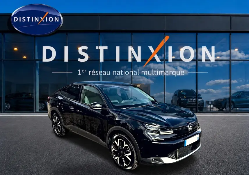 Vue 3/4 avant gauche d'une Citroën C4 X noire 2025 avec jantes alu et calandre distinctive devant un showroom Distinxion.