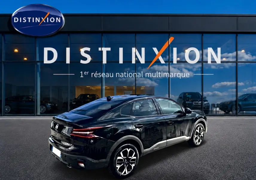 Vue 3/4 arrière droite d'une Citroën C4 X noire 2025 avec jantes alu et feux arrière LED, devant un showroom Distinxion.