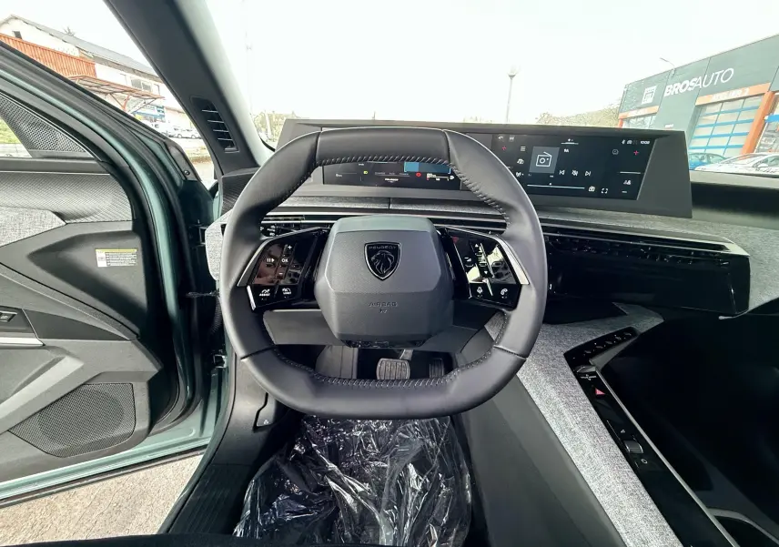Vue intérieure centrée sur le volant du Peugeot 3008 Hybrid 2025, avec tableau de bord numérique et porte conducteur bleu Ingaro Metal ouvert.