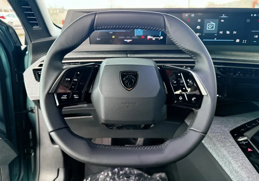 Vue rapprochée du volant cuir noir du Peugeot 3008 Hybrid 2025 avec commandes intégrées et tableau de bord numérique.