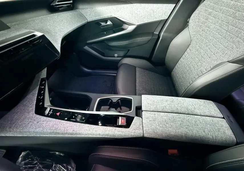 Intérieur avant droit du Peugeot 3008 Hybrid 2025 avec sellerie tissu gris et cuir noir, console centrale moderne et épurée.