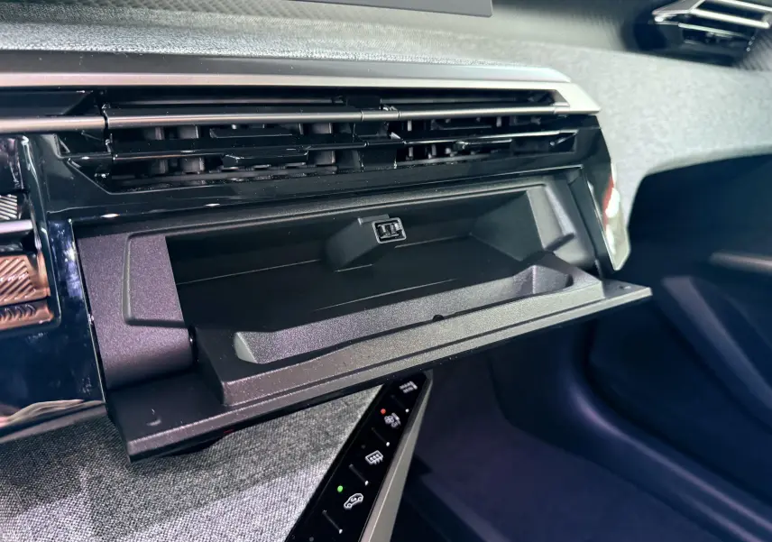 Gros plan sur la boîte à gants ouverte du Peugeot 3008 Hybrid 2025, avec tableau de bord noir et garniture grise.