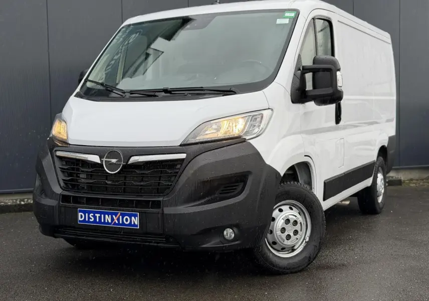 Fourgon Opel Movano blanc en 3/4 avant droit, avec projecteurs allumés et pare-chocs noir robuste visible.