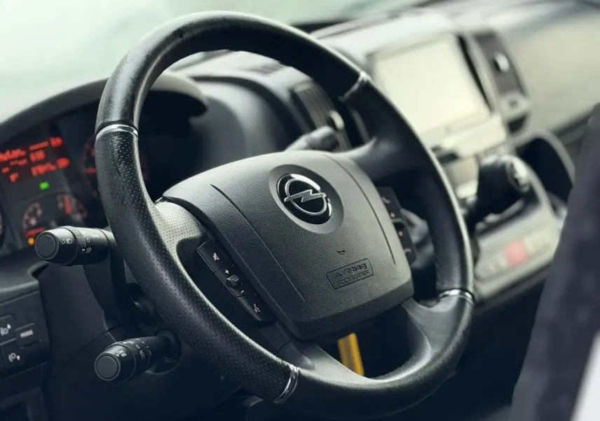 Gros plan sur le volant en cuir noir de l’Opel Movano Fourgon avec tableau de bord et écran tactile flous en arrière-plan.