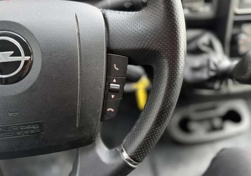 Gros plan sur le volant en cuir noir perforé de l’Opel Movano Fourgon 2024, avec commandes intégrées visibles.