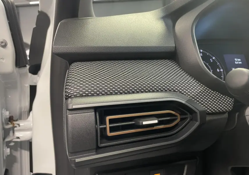 Détail de l'aérateur latéral droit avec insert brun cuivré sur tableau de bord noir et tissu gris de la Dacia Sandero blanche.