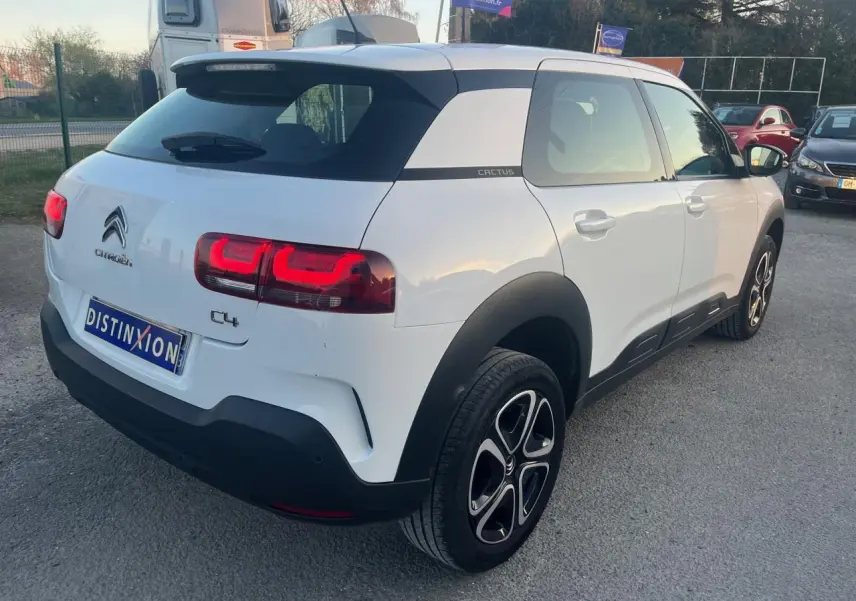 Vue 3/4 arrière droite d'une Citroën C4 Cactus blanche avec protections noires et feux arrière allumés.