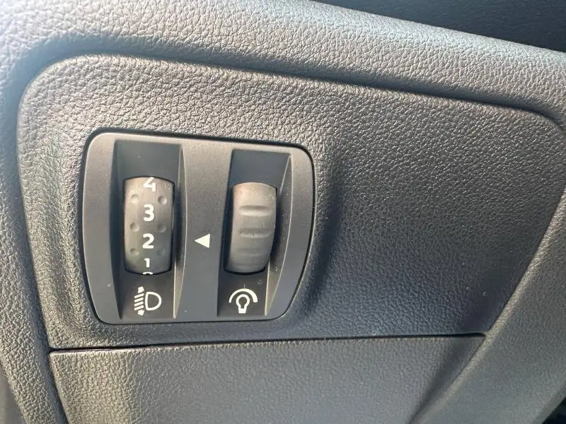 Gros plan sur les commandes de réglage des phares et du tableau de bord d'une Renault Mégane Break gris titanium 2024.