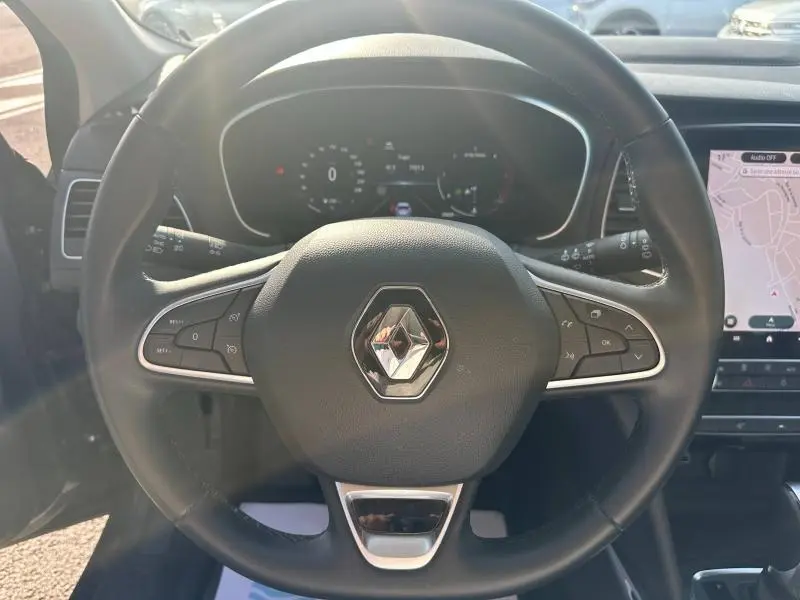 Volant multifonction Renault en cuir noir, vue frontale centrée sur le logo, avec tableau de bord numérique et écran tactile GPS visible.