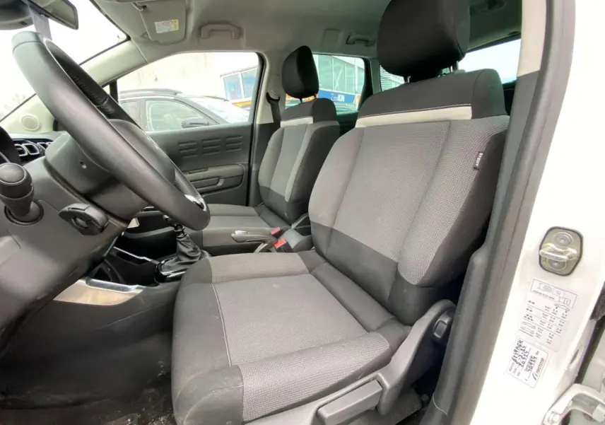 Vue intérieure côté conducteur du Citroën C3 Aircross blanc 2023, montrant les sièges avant en tissu gris et la boîte manuelle.