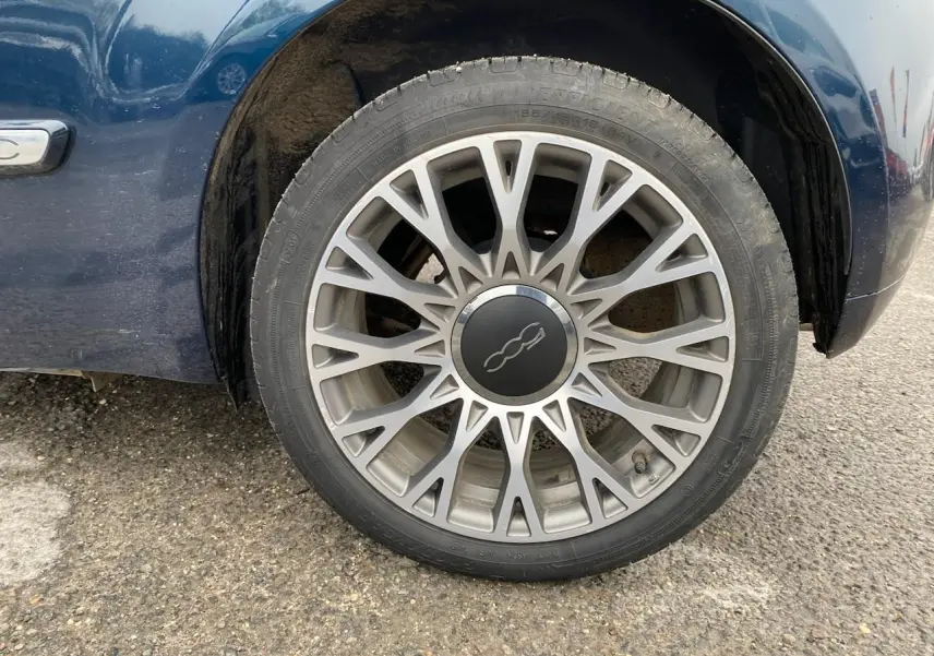 Gros plan sur la roue avant droite d'une Fiat 500 bleu foncé avec jante alliage multibranches distinctive.