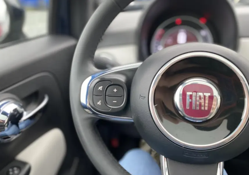 Gros plan sur le volant noir avec logo FIAT rouge et commandes intégrées, intérieur côté gauche de la Fiat 500 2019.