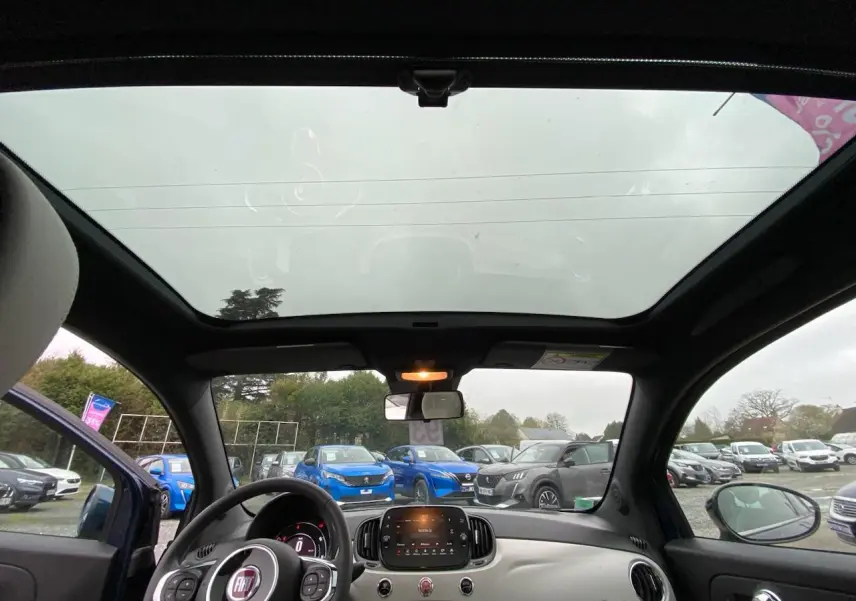 Vue intérieure du toit panoramique et du tableau de bord de la Fiat 500 2019, avec volant noir et tableau de bord clair.
