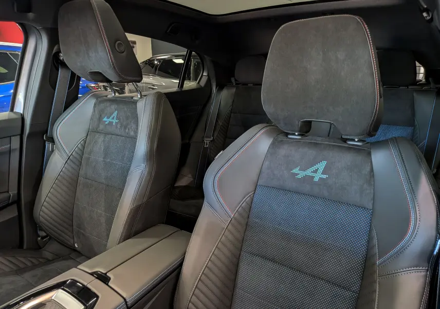 Vue intérieure rapprochée des sièges avant en cuir noir et alcantara avec logo Alpine bleu sur les appuie-têtes.