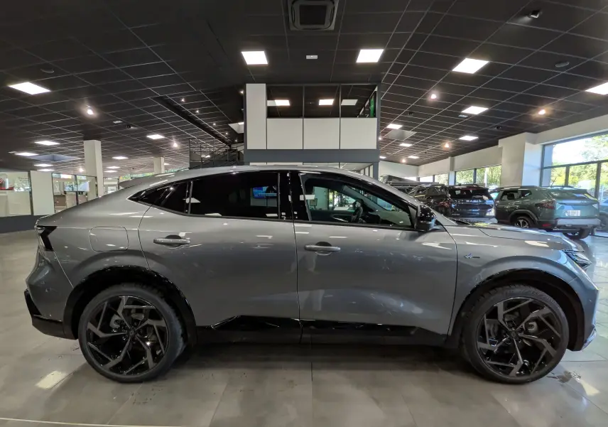 Vue latérale droite d'une Renault Rafale gris schiste, avec jantes noires et lignes fluides dans un showroom lumineux.