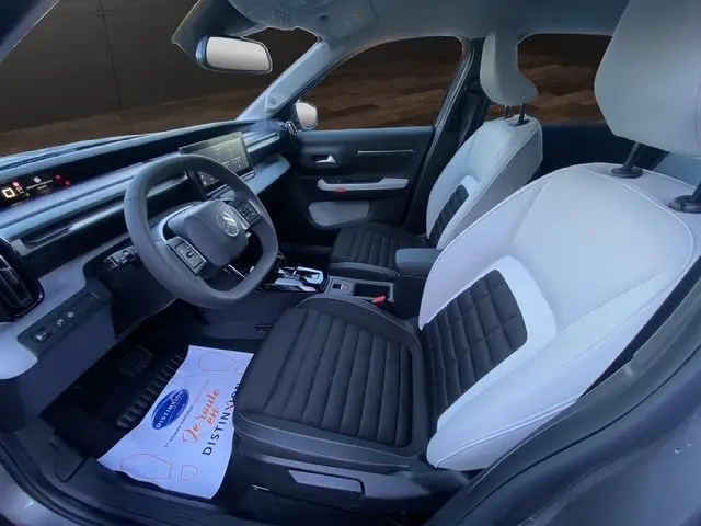 Vue intérieure côté conducteur du Citroën C3 Aircross 2025 hybride, sièges tissu noir et blanc, tableau de bord moderne.