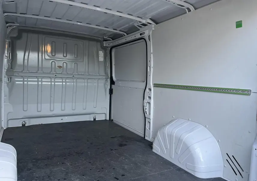 Intérieur du fourgon Opel Movano blanc vu de l'arrière, montrant l'espace de chargement avec plancher et parois métalliques.