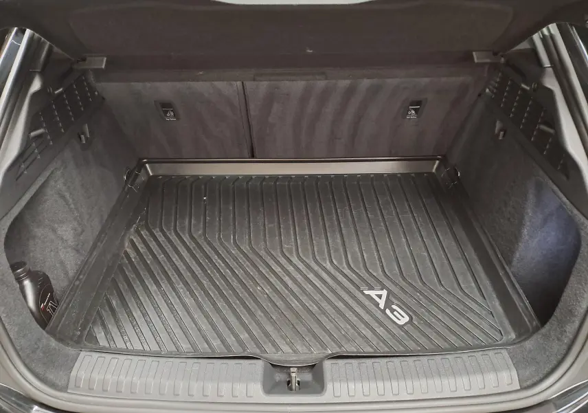 Coffre ouvert de l'Audi A3 Sportback 2023 noir mythic, vue de dessus montrant le tapis de coffre avec logo A3.