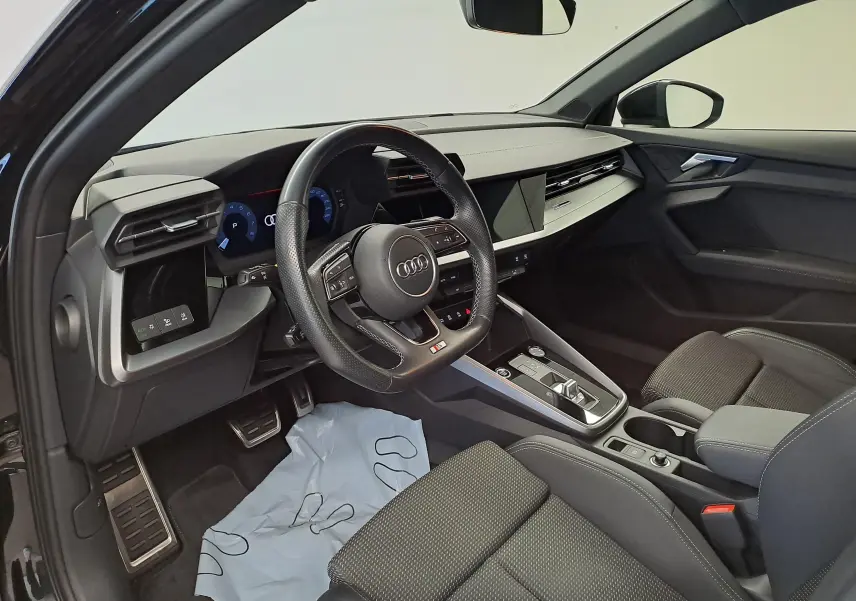 Vue intérieure côté conducteur de l'Audi A3 Sportback 35 TFSI 2023 en Noir Mythic, avec volant multifonction et tableau de bord digital.
