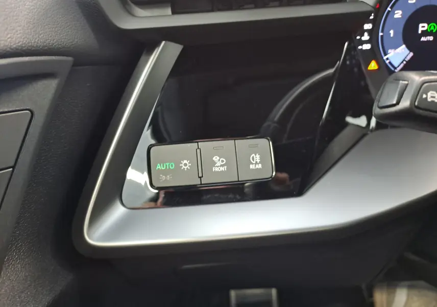 Gros plan sur les commandes d’éclairage à gauche du volant dans l’Audi A3 Sportback noir mythic 2023, version S Line.