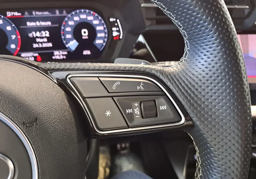 Gros plan sur les commandes au volant côté gauche de l'Audi A3 Sportback 2023 avec tableau de bord numérique en arrière-plan.