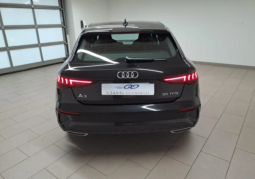 Vue arrière d'une Audi A3 Sportback 35 TFSI 150 S tronic 7 S line noire mythic avec feux LED allumés en intérieur.