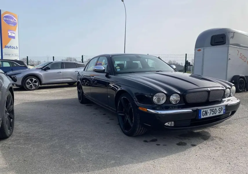 Jaguar XJ noire vue en 3/4 avant droit, avec calandre distinctive et jantes noires brillantes.