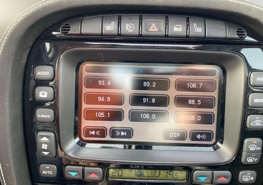Gros plan sur le centre multimédia tactile de la Jaguar XJ noire de 2006, affichant les réglages radio et climatisation.
