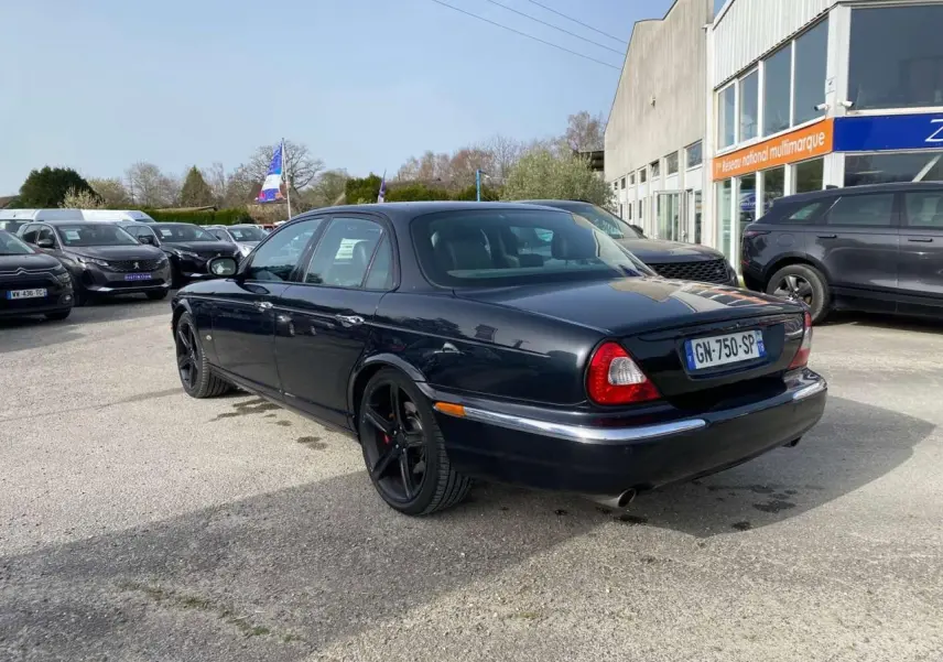 Jaguar XJ noir vue 3/4 arrière droit, avec jantes noires et feux arrière arrondis distinctifs.