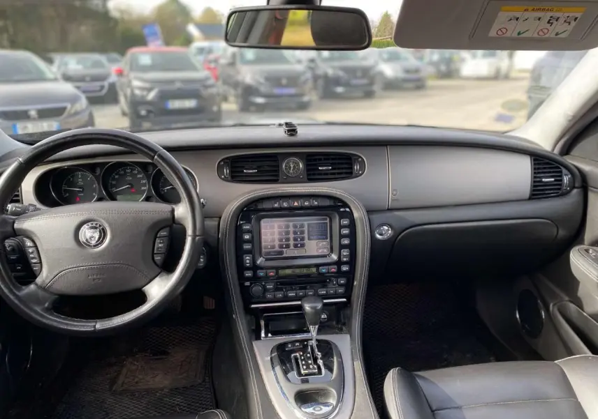 Vue intérieure avant de la Jaguar XJ 2006 noire, montrant le tableau de bord avec écran tactile central et volant cuir.