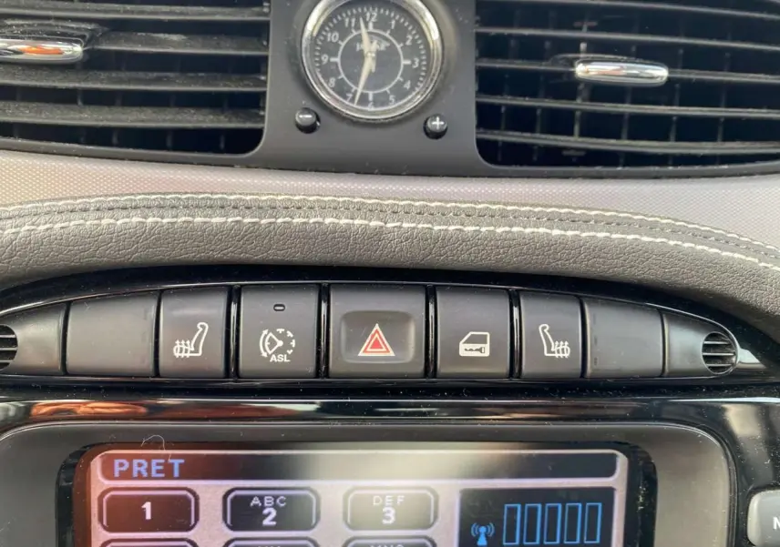 Gros plan sur la console centrale de la Jaguar XJ noire, montrant les boutons de sièges chauffants et l’horloge analogique.