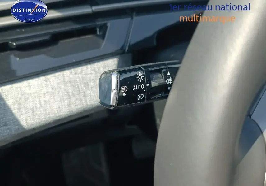 Gros plan sur la commande des phares à gauche du volant d’un Peugeot 5008 gris Artense, intérieur moderne.
