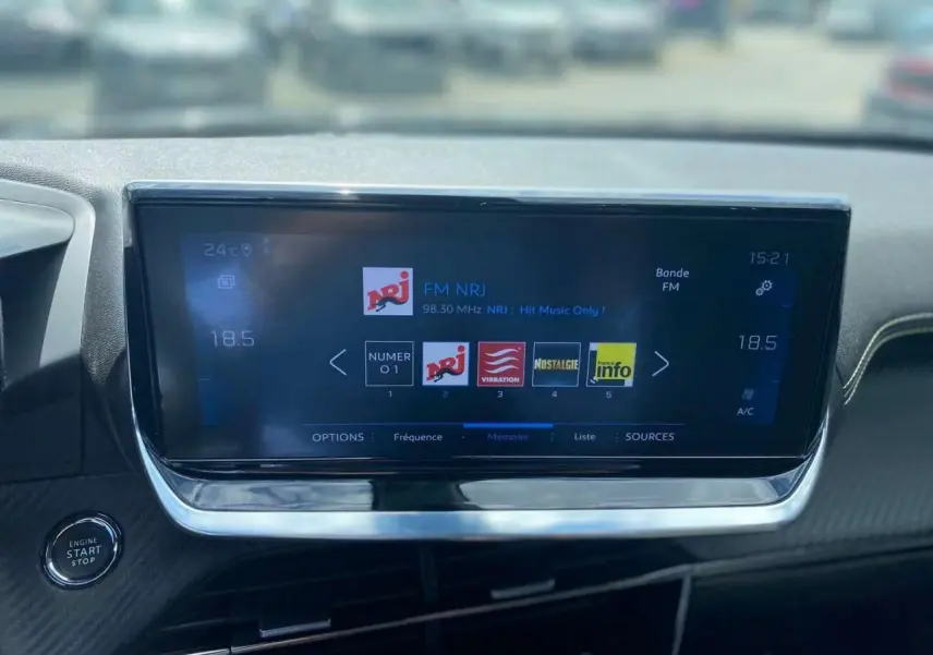 Vue rapprochée de l’écran tactile central de la Peugeot 2008 gris foncé, affichant la radio FM NRJ et le bouton start/stop.