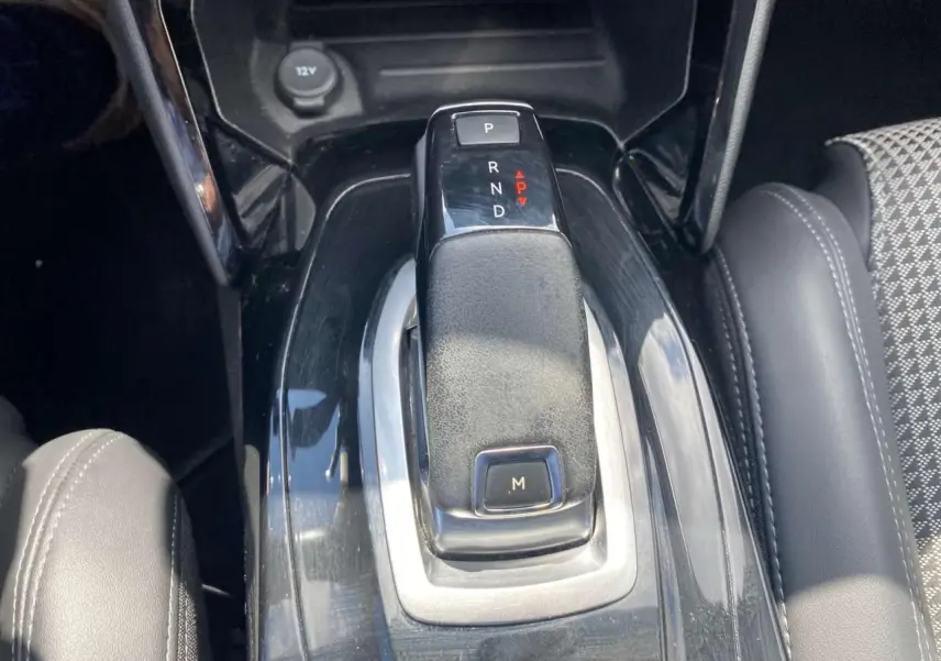 Gros plan sur la commande de boîte automatique noire au centre de la console d'une Peugeot 2008, avec siège gris à droite.