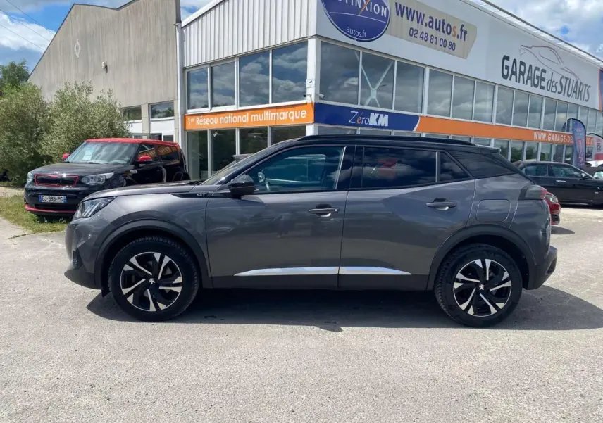 Profil droit d’un Peugeot 2008 GT gris foncé avec toit noir et jantes alliage 17'' bi-tons, stationné devant un garage.