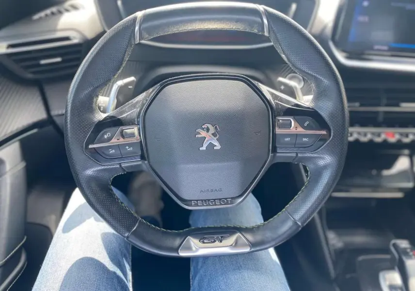 Vue rapprochée du volant cuir noir GT du Peugeot 2008 gris foncé, avec commandes intégrées et logo central.