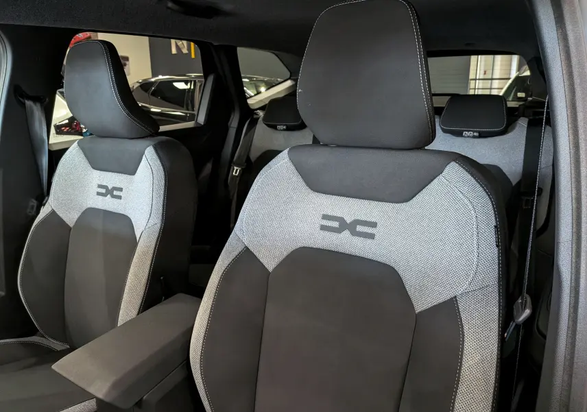 Vue intérieure rapprochée des sièges avant tissu gris et noir du Dacia Bigster 2026 avec logo brodé sur appuie-tête.