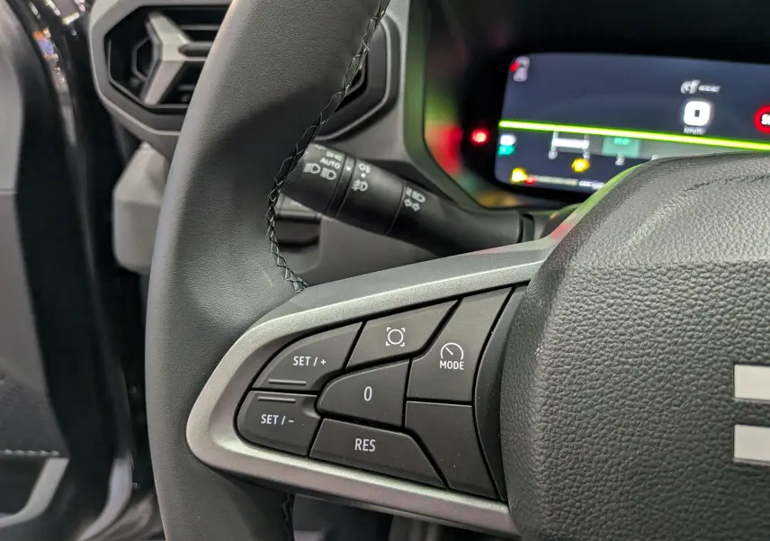 Gros plan sur les commandes au volant du Dacia Bigster 2026, intérieur noir avec affichage numérique en arrière-plan.