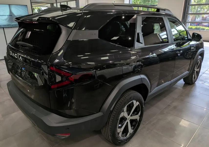 Vue 3/4 arrière droite du Dacia Bigster noir nacré 2026 avec jantes bicolores et vitres teintées en showroom.