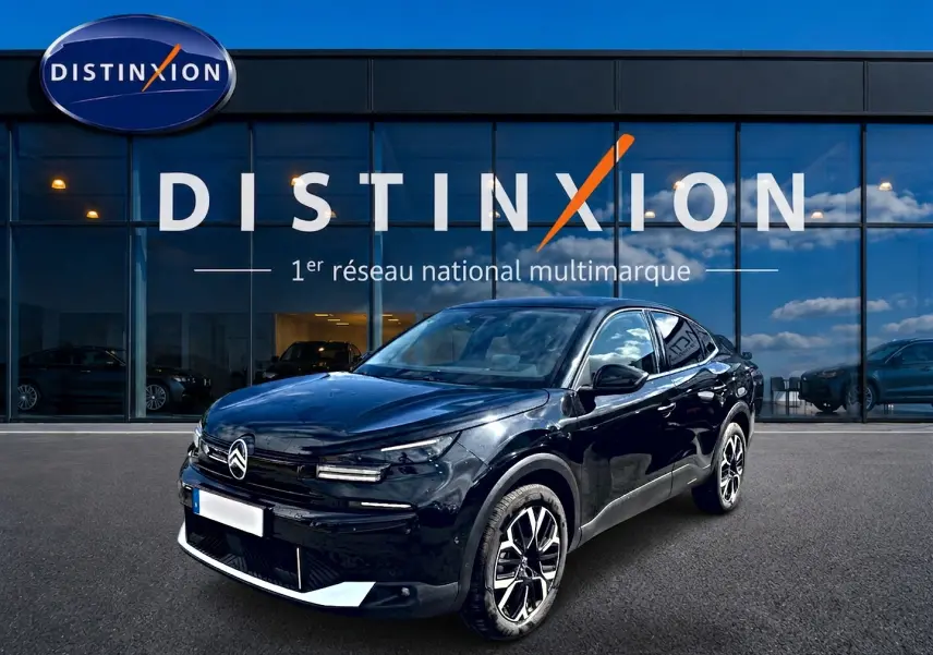 Citroën C4 X noire vue 3/4 avant droit, avec jantes alu distinctives, devant une vitrine Distinxion.