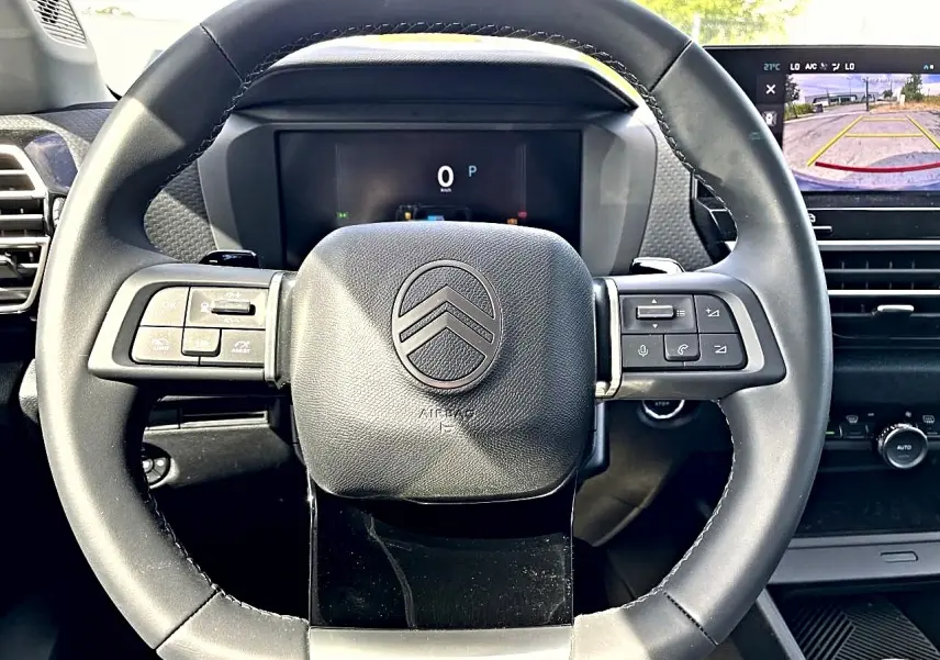 Vue rapprochée du volant cuir noir de la Citroën C4 X 2025 avec commandes intégrées et écran de caméra de recul visible.