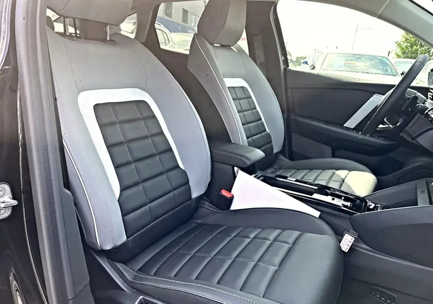 Vue intérieure côté conducteur de la Citroën C4 X noire 2025, sièges bi-matière gris et noir avec accoudoir central.