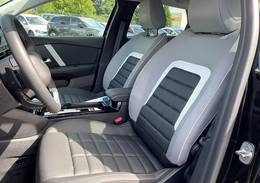 Vue intérieure côté conducteur de la Citroën C4 X noire 2025, sièges bi-tons gris et noir avec accoudoir central.