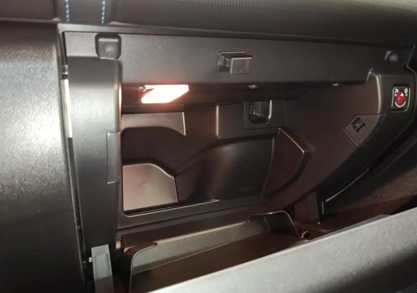 Vue rapprochée de la boîte à gants ouverte du Citroën C5 Aircross 2024, éclairage intérieur visible, plastique noir mat.